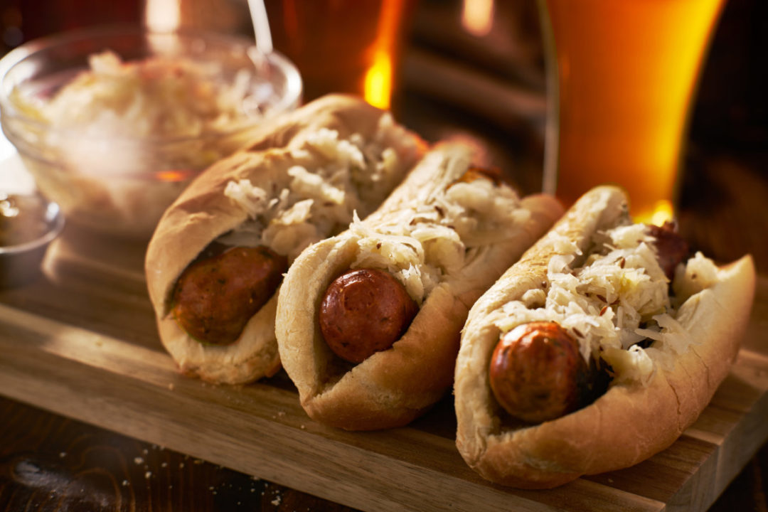 Three beer bratwursts in hot dog buns covered in sauerkraut