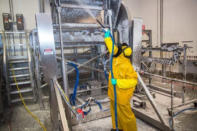 Worker using disinfectant foam to clean processing plant