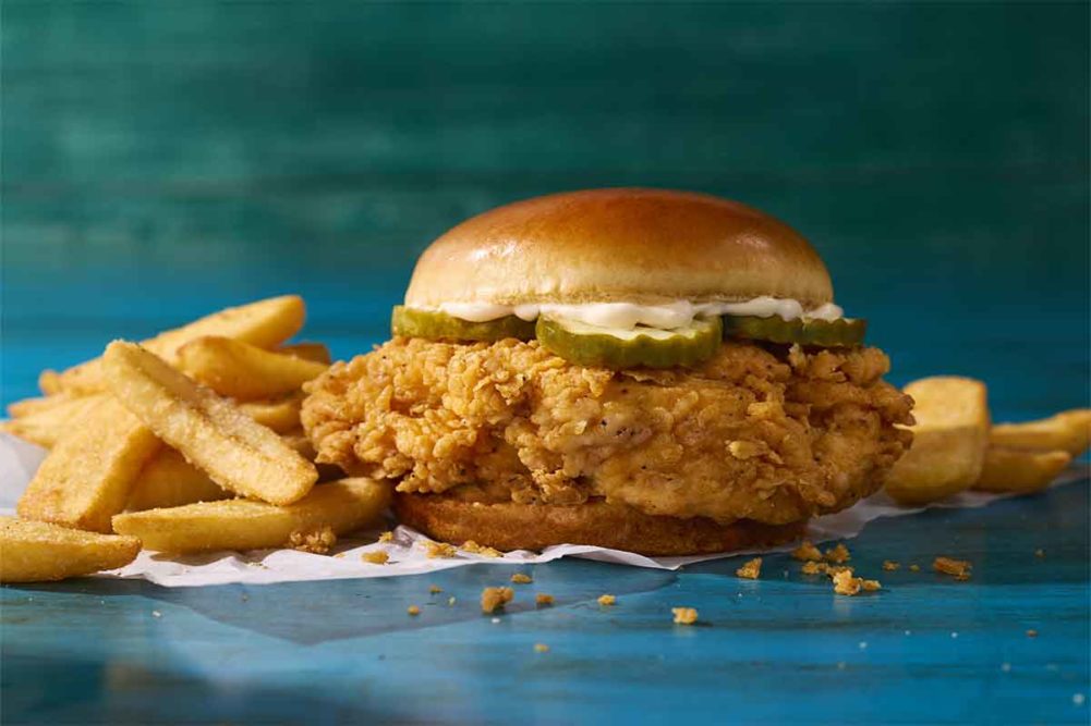 Fried chicken breast filet on brioche bun topped with pickles and mayonnaise next to a pile of french fries