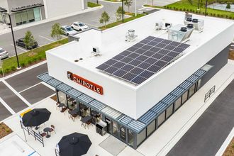 Rendering of Chipotle Mexican Grill restaurant with solar panels on the roof, drive thru lane and tables with red umbrellas near the entrance.