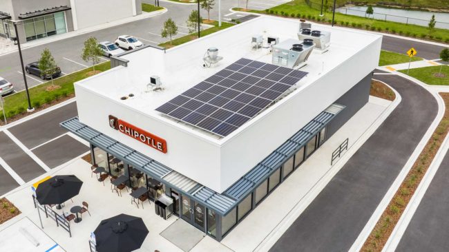 Rendering of Chipotle Mexican Grill restaurant with solar panels on the roof, drive thru lane and tables with red umbrellas near the entrance.