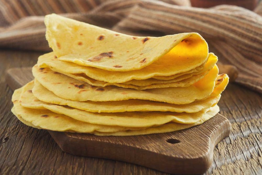corn tortillas stacked on a brown wood cutting board